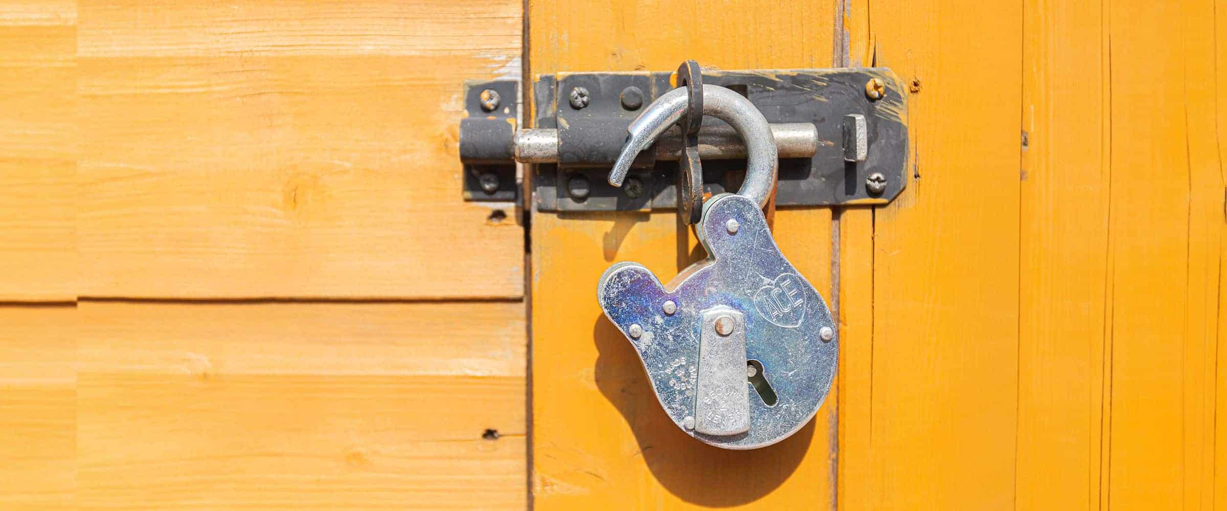 an unlocked padlock hooked to a deadbolt on a door.